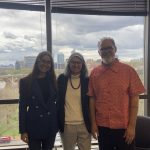 Visiting Researchers Lutiana Valadares and Carlos Faria pose with visiting Ruth Cardoso Fulbright Chair in Brazilian Studies Carmen Rial in front of the windows of the Murray Room in Lauinger Library, with a cloudy view of Washington, DC behind them.